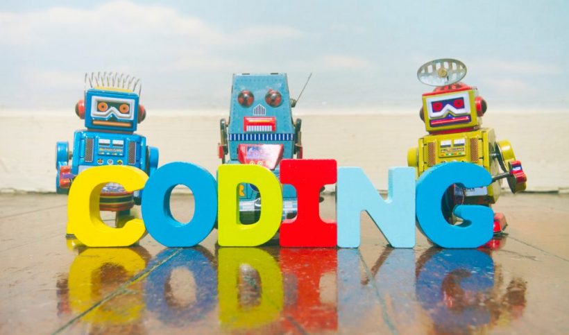 Three robots on a beach, in front of them is letters spelling coding.