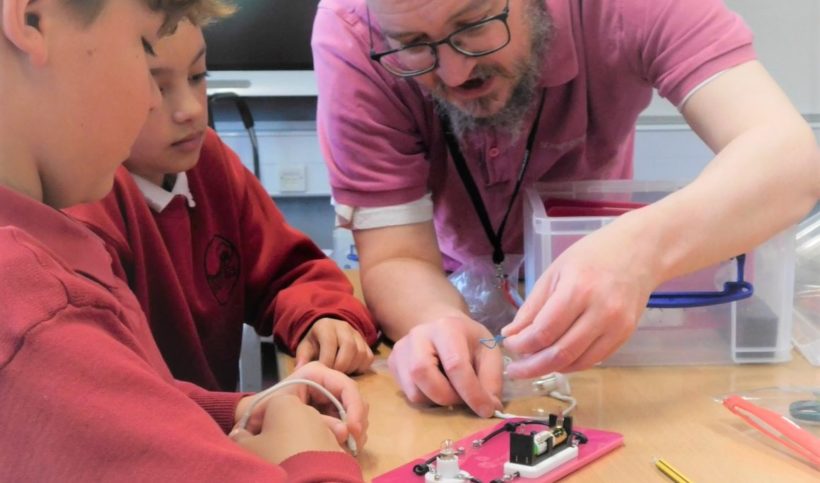 A man helping two boys with electric circuit kit