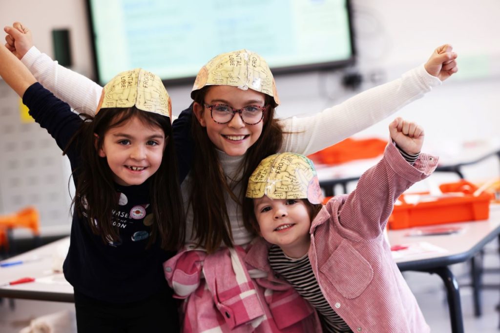 3 young girls with map of brain as hats, raising hands in cheer