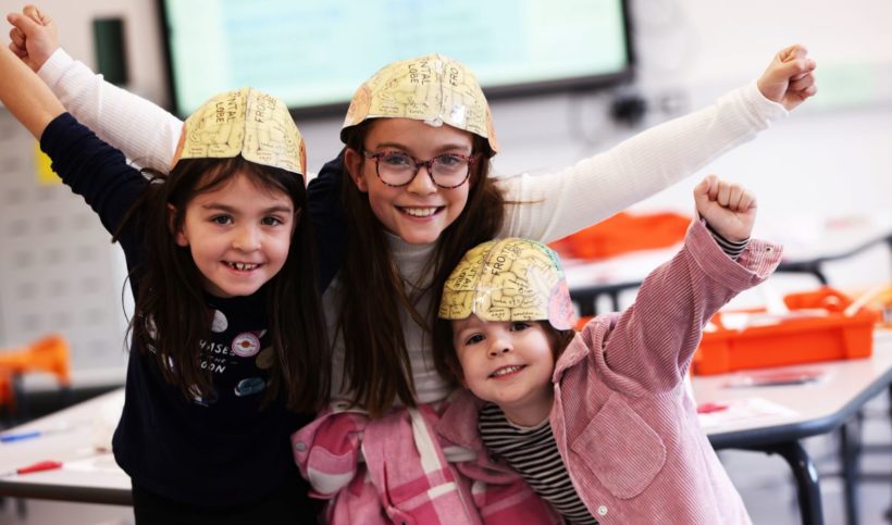 3 young girls with map of brain as hats, raising hands in cheer