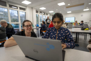 Here image: Child and Club leader in workshop at laptop