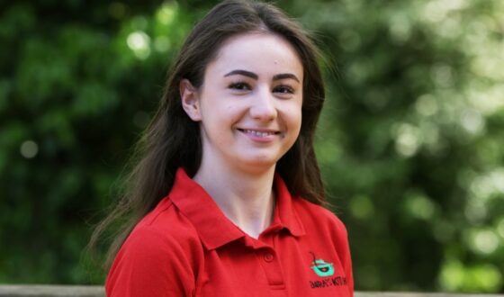 Head and shoulder profile photo of cafe team member, with green foliage background