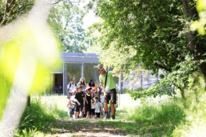 Group of young school children in woodland with 2 teachers, and man pointing for them to look at something