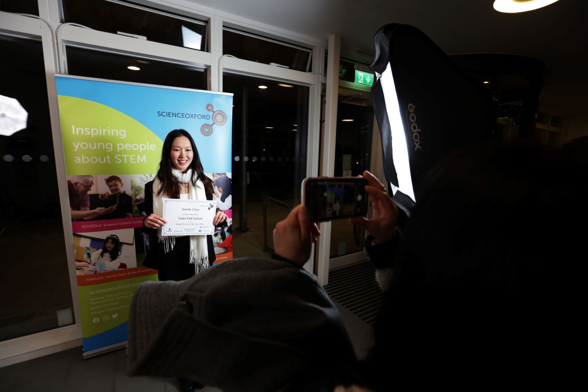 Young person standing in front of colourful Science Oxford banner having photos taken