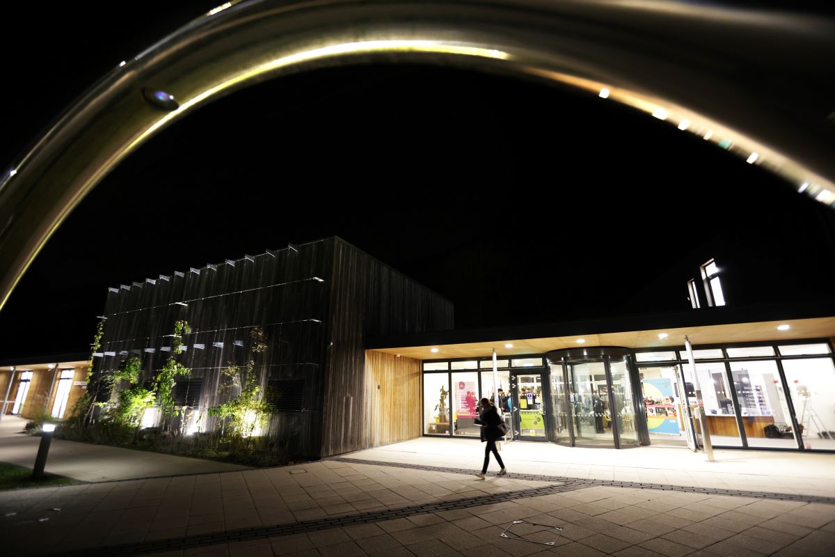 Photo of building lit at night, taken through the arch of an ohm statue