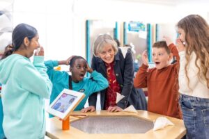 Group of 4 children and 1 adult around science exhibit, showing gasps of delight